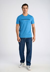 Blå melerad t-shirt med rund hals och svart text "COPENHAGEN LINDBERGH". Kombinerad med mörka jeans och vita sneakers.