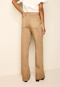 Hiekansävyiset leveälahkeiset housut, joissa korkea vyötärö, kaksi takataskua ja sileä pinta. Kangas on hieman kiiltävä ja muotoiltu rentoon istuvuuteen.