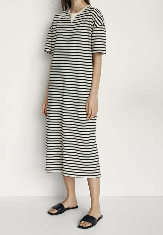 Femme debout portant une robe midi à rayures horizontales noires et blanches, manches courtes et sandales noires à bout ouvert.