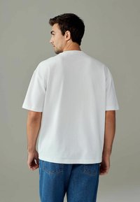 Hvid kortærmet t-shirt i bomuldsstof, afslappet pasform. Bæres med blå denim jeans. Minimalistisk design, ingen synlige mønstre eller logoer.