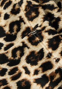 Leopardmønstret stoff med en blanding av beige, svart og brune flekker på en teksturert overflate, med synlige sømmer og folder.