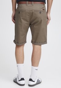 Pantalones cortos de algodón marrones con puños enrollados, que cuentan con dos bolsillos traseros y una etiqueta de cuero. Combinados con calcetines blancos y zapatillas negras y blancas.