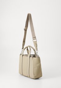Beige tote bag made of soft material, featuring two top handles and an adjustable shoulder strap. Smooth surface with a zipper closure.