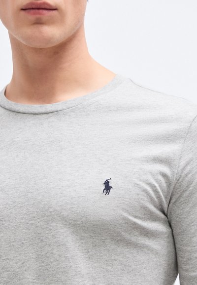 Šedé bavlněné tričko s kulatým výstřihem a malým námořnicky modrým logem polo na levé straně hrudníku. Materiál má hladkou, měkkou texturu.