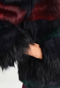 Faux fur jacket featuring black, burgundy, and green horizontal stripes, with long, soft texture. The sleeve extends to the wrist.