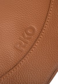 Ruskea textured-nahka, jossa on painettu "RKO" -logo, ja reunassa kevyt ommel. Pintamateriaali osoittaa hienovaraisen puuvillakuvion.