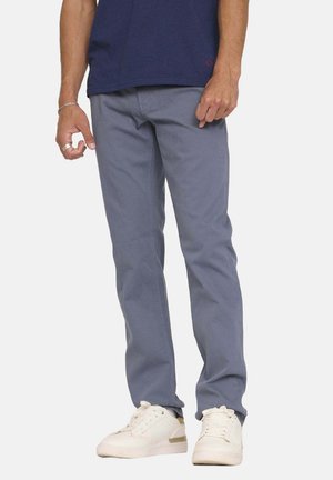 Pantalon en coton gris à coupe droite, avec poches latérales et détails de couture subtils. Associé à des baskets blanches.