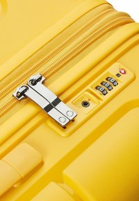Harde gele koffer met textuur, dubbele ritsen en een combinatie slot. Beschikt over platte hardware en gevormde accenten.
