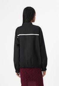 Black bomber jacket with a high collar, ribbed cuffs, and elastic hem; features a white horizontal stripe across the upper back.