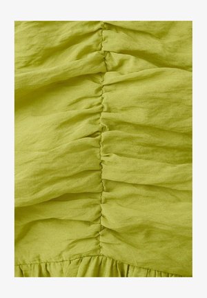 Jasně zelená látka s těsnými svislými záhyby vytvářejícími texturované, nařasené sklady uprostřed.