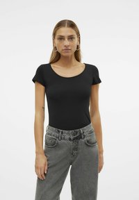 Body noir à manches courtes avec un col rond, associé à un jean gris taille haute avec une texture délavée et des poches avant.