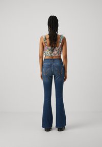 Cvjetni crop top s volanima na naramenicama, uparen s rozim trapericama koje imaju stražnje džepove i kontrastne šavove. Crne platforme.