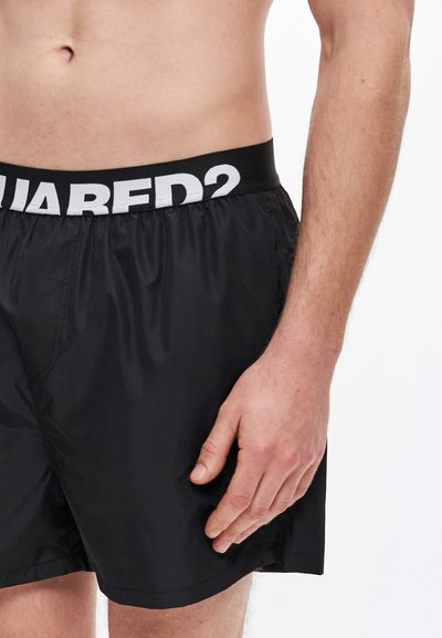 Bañador corto negro con cinturilla elástica y logotipo blanco. La tela parece ligera y suave, con un ajuste holgado.