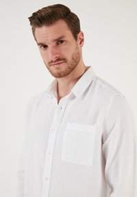 Fehér gombos ing, texturált anyagból készült, mellzsebbel és klasszikus gallérral, kényelmesebb szabású. 