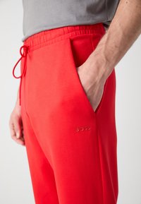 Rode sweatpants met een elastische tailleband en trekkoord, voorzien van een zijzak en een gegraveerd logo op de bovenbeen. Glad katoenen stof.