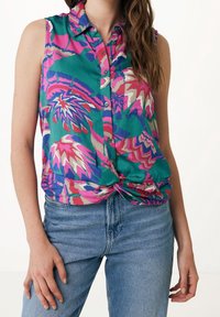 Blouse sans manches verte avec des motifs floraux roses, violets et crème, dotée d'un col, d'une fermeture à boutons et d'un détail torsadé à l'ourlet.