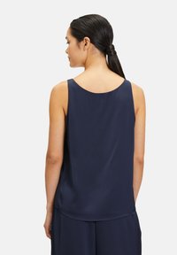 Granatowa, bezrękawnikowa bluzka z jedwabistego materiału o okrągłym dekolcie i luźnym kroju, charakteryzująca się gładką teksturą i subtelnym opadającym fasonem.