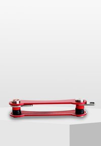 Multi-outil rouge en métal avec deux accents circulaires argentés et des poignées en caoutchouc noir, présentant un design slim et allongé avec une forme courbée.