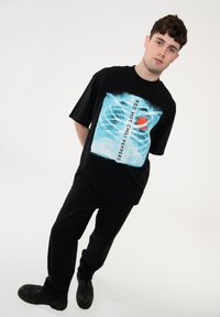 Black oversized t-shirt featuring a graphic print of blue ribs and a red chili pepper with text “RED HOT CHILI PEPPERS” in a bold font.