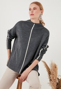 Gray knitted sweater with a high collar, featuring a vertical white stripe and white accents on sleeves. Relaxed fit, soft texture.