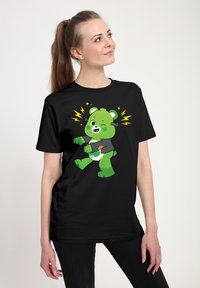 Camiseta negra con un oso de dibujos animados verde que guiña un ojo y tiene acentos en forma de rayo. El oso lleva una camiseta gris y presenta patrones juguetones.