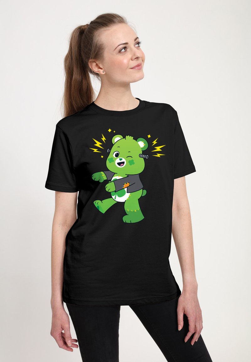 Camiseta negra con un oso de dibujos animados verde que guiña un ojo y tiene acentos en forma de rayo. El oso lleva una camiseta gris y presenta patrones juguetones.