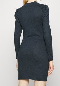 Mörkblå långärmad klänning med en figursydd form, tillverkad av ett texturerat tyg. Har samlade detaljer vid axlarna.