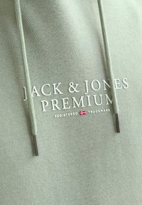 Svetlozelená mikina s štruktúrovaným povrchom, vybavená bielym logom "JACK & JONES PREMIUM" a striebornými prackami na šnúrkach.
