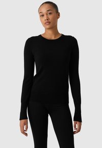 Černý pletený svetr s dlouhými rukávy, kulatým výstřihem a přiléhavým střihem. Měkká textura s jemnými švy a mírně rozšířenými manžetami.