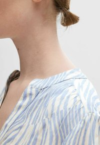 Camicetta a righe blu e bianche con colletto; il tessuto sembra leggero. Presenta un design semplice con cuciture e texture visibili.