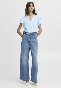 Blusa azzurra a maniche corte con un motivo a pois testurizzato, abbinata a jeans in denim blu a vita alta e gamba larga e tacchi color crema.