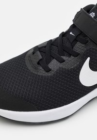Chaussure de sport noire avec une tige en mesh texturé, des lacets noirs, un col rembourré et un logo Nike Swoosh blanc. Elle dispose d'une semelle blanche en caoutchouc.