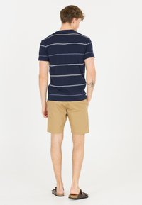 Laivastonsininen raidallinen t-paita lyhyillä hihoilla, yhdistetty khaki-shortseihin. Mallilla on päällä ruskeat liukuvoimistelukengät. Minimalistinen muotoilu ja pehmeä kangas.