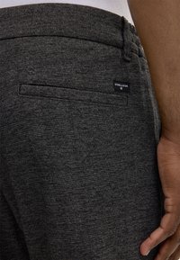 Pantaloni grigi con texture, caratterizzati da una tasca posteriore, un'etichetta Strellson e una vestibilità sartoriale. Il tessuto presenta un sottile motivo intrecciato.