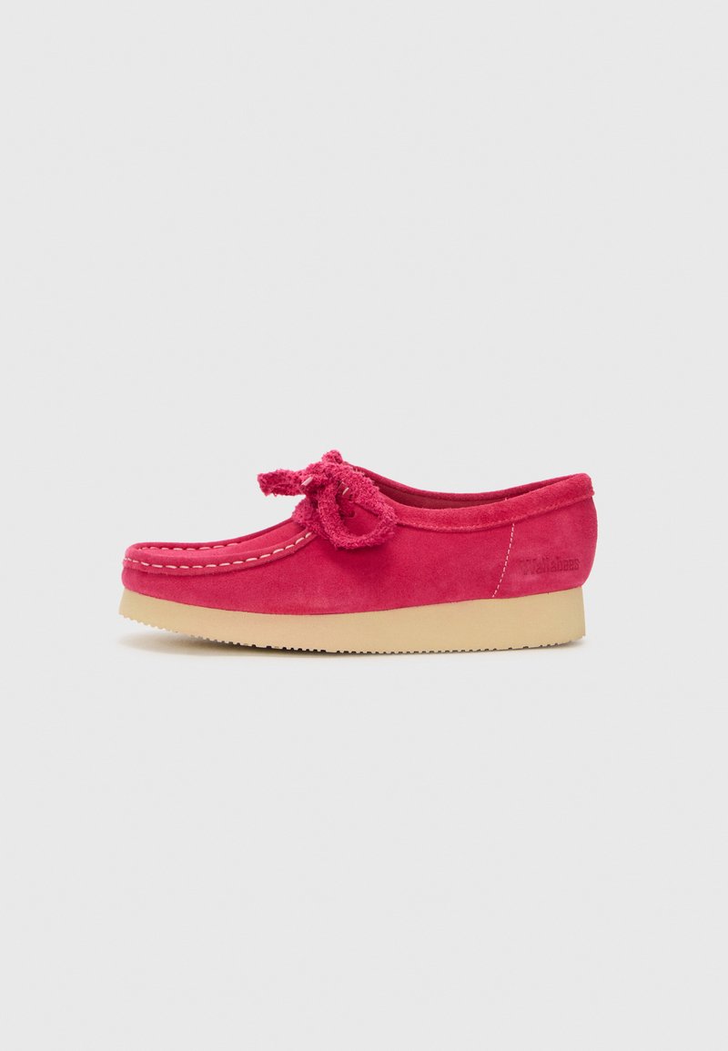 Scarpa slip-on in suede rosa con punta rotonda, fiocco decorativo sulla parte anteriore e suola in gomma beige. Presenta una cucitura bianca lungo il bordo.