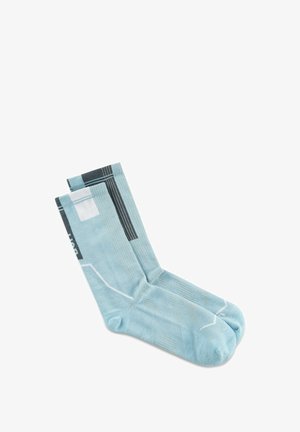 Hellblaue Knöchelsocken mit schwarzen, weißen und grauen geometrischen Mustern, flach auf einem weißen Hintergrund ausgelegt.