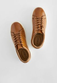 Baskets en cuir marron avec semelles en caoutchouc blanches, dotées de lacets plats, d'un bout arrondi et de détails de couture minimalistes.