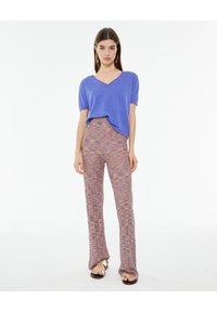 Purple short-sleeve V-neck top paired with multicolored textured long pants featuring a relaxed fit. Simple sandals complete the outfit.