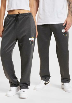 Hallide hallid püksid elastse vöökoha ja nööriga, vasakul reiel graafilise logoga. Koos valgete tennistega.