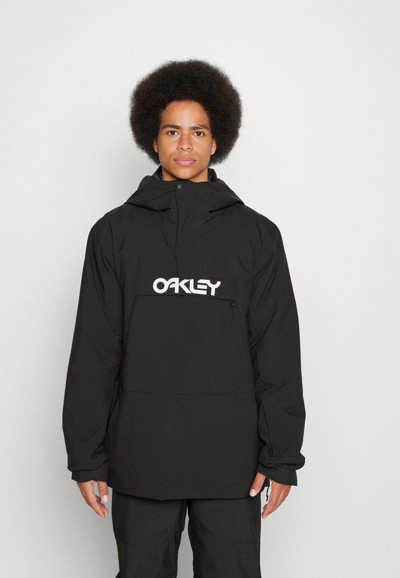 Czarna wodoodporna kurtka z kapturem, z dużą kieszenią z przodu i przerośniętym białym logo "OAKLEY". Teksturowany, lekki materiał.