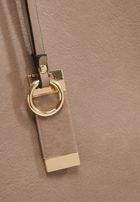 Beiges l�äderetikett med en guldtonad ring och beslag fästa med ett svart band. Texturerad yta med en slät finish.