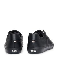 Schwarze Ledersneaker mit glatter Textur, runder Form, Gummisohle und auffälligem "BOSS"-Logo an der Ferse. Keine zusätzlichen Akzente sichtbar.