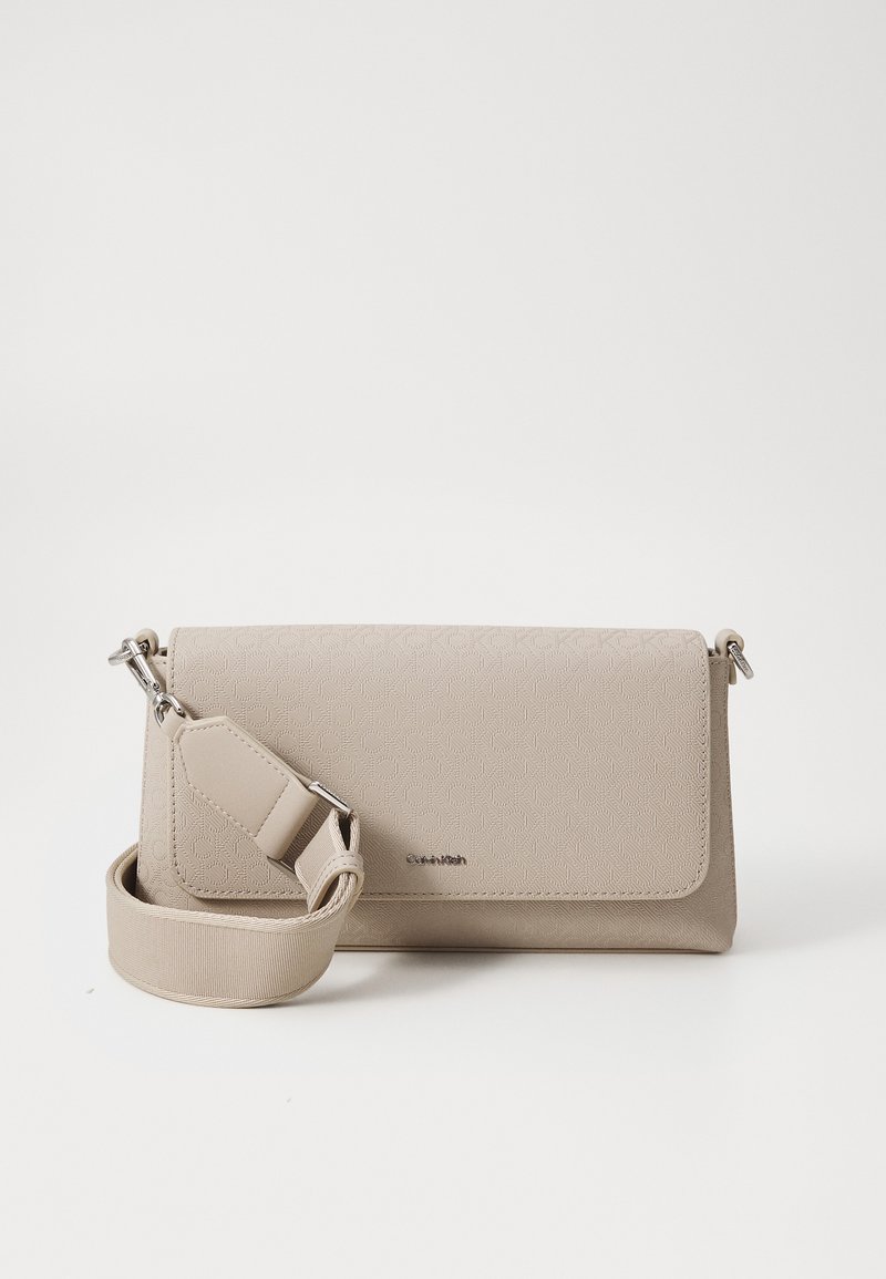 Sac bandoulière beige en matériau texturé avec un rabat, une sangle ajustable et un motif subtil. Comprend des accents en métal argenté.