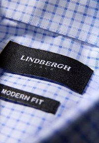 Tessuto a quadretti azzurro chiaro e bianco con etichette nere riportanti "LINDBERGH" e "MODERN FIT". Texture liscia con colletto strutturato.