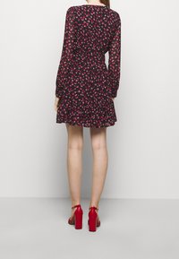 Vestido negro con un patrón floral en rosa y verde, mangas largas, dobladillo con volantes, combinado con sandalias rojas de tacón bloque.