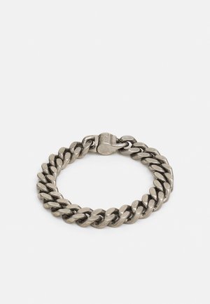 Massives silbernes Kettenarmband mit einem pfeifenförmigen Verschluss, der mit dem Markennamen "GUESS" graviert ist, vor weißem Hintergrund.