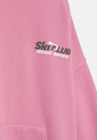 Felpa rosa con vestibilità comoda. Presenta i loghi "Ski Club" e "Winter Series" in grigio scuro e bianco. Tessuto morbido, dettagli minimali.