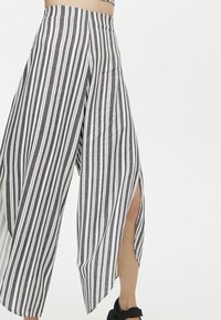 Gestreepte wijde broek in zwart-witte stof, met een hoge split aan elke kant en een aansluitende tailleband.