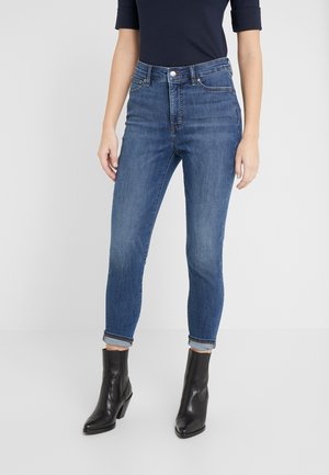 Slim-fit blå jeans med op rullede manchetter, båret med sorte mellemlange støvler med hæl og en navyblå top med albuelange ærmer.
