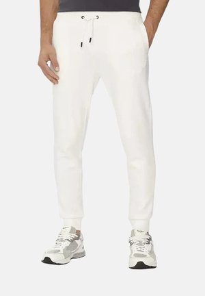 Homme portant un pantalon de jogging blanc avec taille à cordon et des baskets blanches et grises, debout les mains dans les poches.